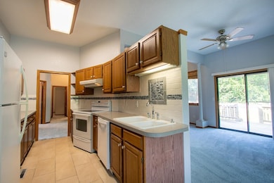 Kitchen with white appliances, light colored carpet, tasteful backsplash, light countertops, and a ceiling fan