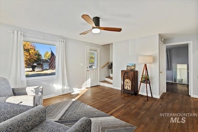 Sitting room with dark wood-style floors, ceiling fan, and stairs