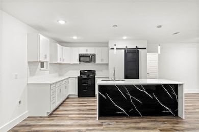 Kitchen featuring a barn door, tasteful backsplash, black appliances, decorative light fixtures, and light stone counters