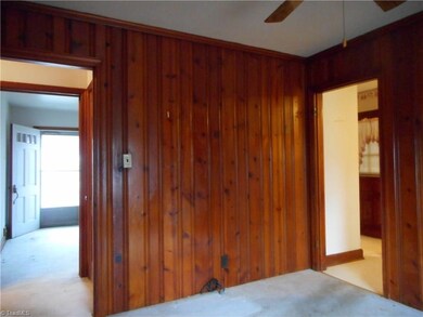 Dining Room: Room features include knotty pine covered walls, a window for natural lighting, a ceiling fan and crown molding. The open door on the right side is to the kitchen and breakfast areas. The open door on the left side is to the main hallway and bedrooms with the living room at the far end.