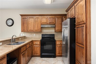 Kitchen featuring light tile patterned flooring, electric range, sink, stainless steel fridge, and backsplash