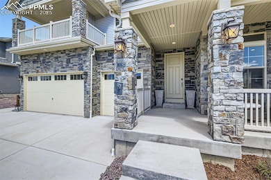Property entrance featuring a balcony, stone siding, an attached 3 car garage, and driveway