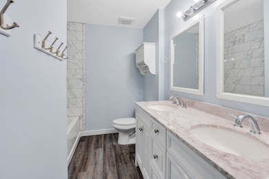 Full bathroom featuring double vanity, dark wood finished floors, and shower / bathtub combination