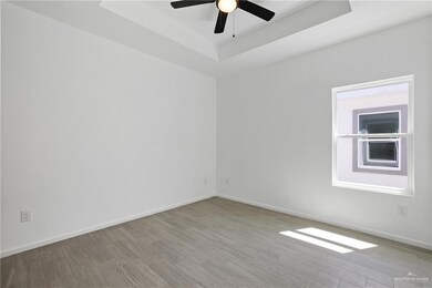 Unfurnished room with a raised ceiling, wood finished floors, ceiling fan, and baseboards