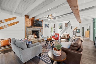 Living area featuring beam ceiling, wood walls, a stone fireplace, stairs, and wood finished floors