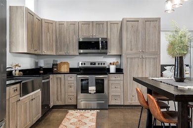 Kitchen featuring appliances with stainless steel finishes, concrete floors, and dark stone counters