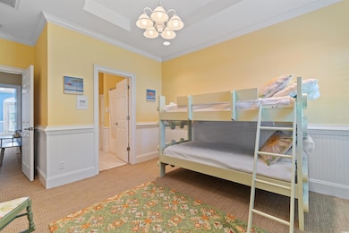 Bedroom featuring carpet flooring, a chandelier, crown molding, a wainscoted wall, and ensuite bathroom