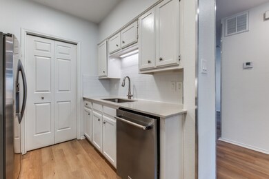 Kitchen featuring light wood-style floors, stainless steel appliances, white cabinets, and decorative backsplash