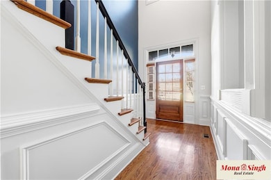 Foyer entrance with stairs, dark wood-style floors, a wainscoted wall, and a decorative wall