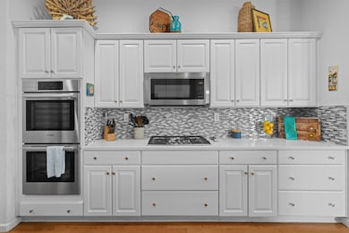 kitchen with appliances with stainless steel finishes, white cabinets, decorative backsplash, and light stone counters