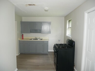 Kitchen with black gas range, a sink, gray cabinets, wood finished floors, and baseboards
