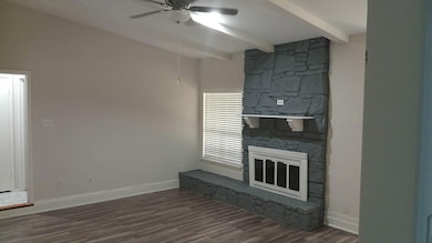 Unfurnished living room with dark wood-style flooring, beamed ceiling, ceiling fan, and a fireplace
