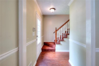 Foyer entrance with wood finished floors, stairway, a textured ceiling, and crown molding