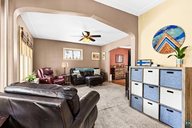 Carpeted living room featuring arched walkways, ceiling fan, and plenty of natural light