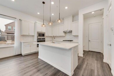 Kitchen featuring white cabinetry, a center island with sink, stainless steel appliances, decorative light fixtures, and sink