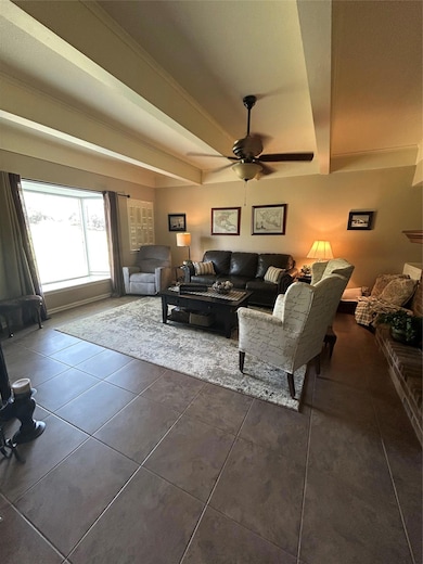 Tiled living area featuring ceiling fan and beamed ceiling
