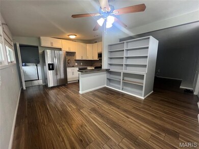 Kitchen with dark countertops, backsplash, white cabinets, appliances with stainless steel finishes, and dark wood-type flooring