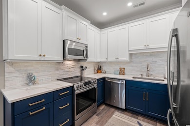 Kitchen with a sink, appliances with stainless steel finishes, visible vents, white cabinets, and blue cabinetry