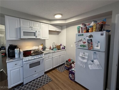 Kitchen with white appliances, a textured ceiling, white cabinetry, dark wood-type flooring, and tasteful backsplash