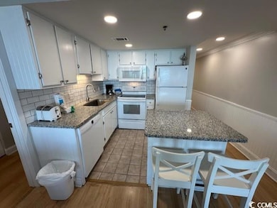 Kitchen featuring white appliances, sink, white cabinets, dark stone countertops, and light hardwood / wood-style flooring