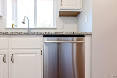 Kitchen view of stainless steel dishwasher, white cabinetry, tasteful backsplash, and light stone counters
