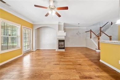 Unfurnished living room featuring a ceiling fan, light wood finished floors, crown molding, a fireplace, and arched walkways