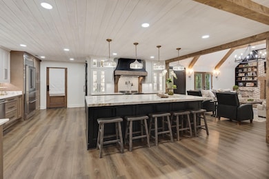 Kitchen with a kitchen breakfast bar, hanging light fixtures, glass insert cabinets, light stone countertops, and dark wood-type flooring