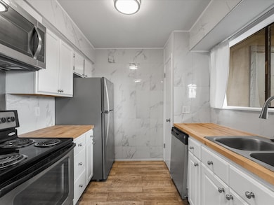 Modern kitchen featuring sleek stainless steel appliances, elegant marble-patterned walls, and warm wood countertops. Abundant natural light and ample storage make it both stylish and functional.