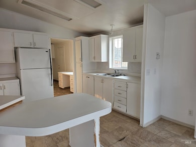 Kitchen with light countertops, freestanding refrigerator, and white cabinetry
