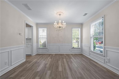 Unfurnished dining area featuring a chandelier, wood finished floors, a wainscoted wall, crown molding, and a decorative wall