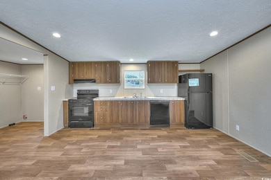 Kitchen with light wood-style floors, ornamental molding, brown cabinetry, and black appliances