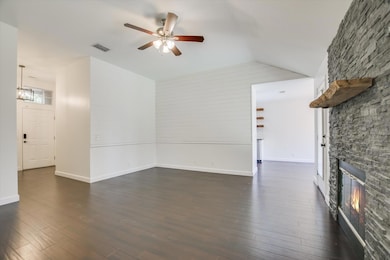 Unfurnished living room with dark wood finished floors, a fireplace, ceiling fan, and vaulted ceiling
