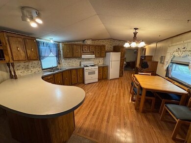 Kitchen featuring vaulted ceiling, white appliances, a peninsula, light wood-style floors, and pendant lighting