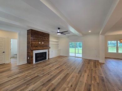 Unfurnished living room with beamed ceiling, a gas fireplace, ceiling fan, LVP floors, and custom built-ins.