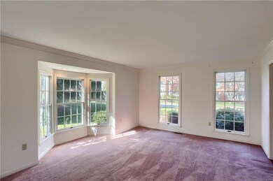 The generously sized living room boasts sun filled windows, including a bay, crown molding and carpet.