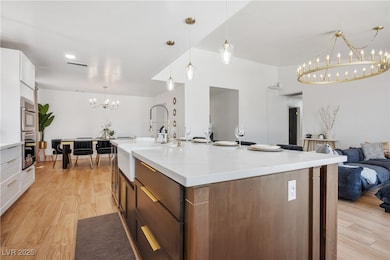 Kitchen featuring a chandelier, decorative light fixtures, white cabinets, open floor plan, and light wood-type flooring
