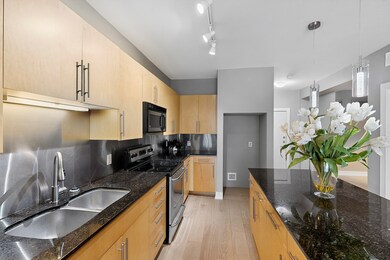 Kitchen featuring electric range, black microwave, light brown cabinets, light wood finished floors, and pendant lighting