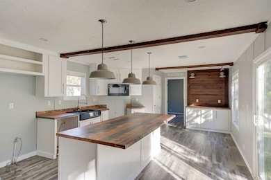 Kitchen featuring white cabinetry, hanging light fixtures, beamed ceiling, dark wood finished floors, and butcher block countertops