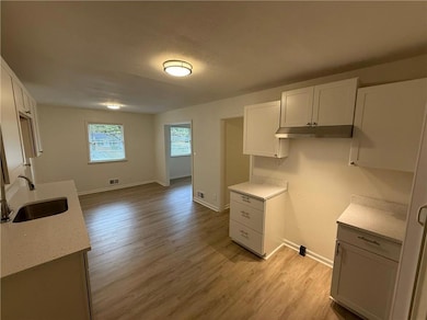 Kitchen with light stone counters, light wood-type flooring, white cabinets, a textured ceiling, and under cabinet range hood