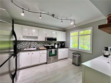 Kitchen featuring appliances with stainless steel finishes, ornamental molding, backsplash, white cabinets, and dark countertops