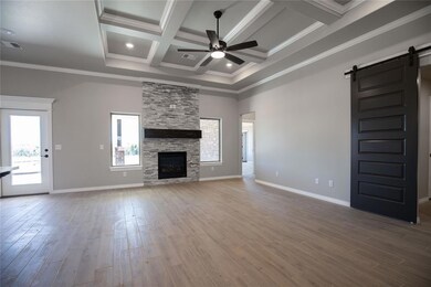 Unfurnished living room with coffered ceiling, a barn door, hardwood / wood-style flooring, a stone fireplace, and ceiling fan
