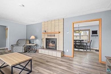 Living area with wood finished floors, a chandelier, a brick fireplace, and crown molding