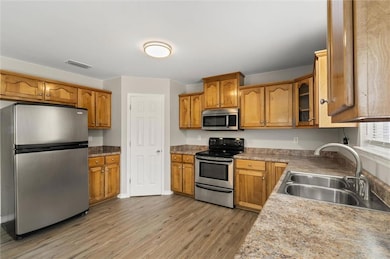 Kitchen with appliances with stainless steel finishes, light wood-style flooring, brown cabinetry, and glass insert cabinets