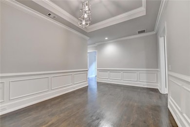 Empty room featuring a tray ceiling, dark wood-type flooring, and ornamental molding