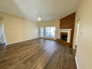 Unfurnished living room with a brick fireplace, dark wood-style flooring, ceiling fan, and a textured ceiling
