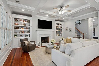 Living area featuring dark wood finished floors, ceiling fan, coffered ceiling, a fireplace with flush hearth, and crown molding