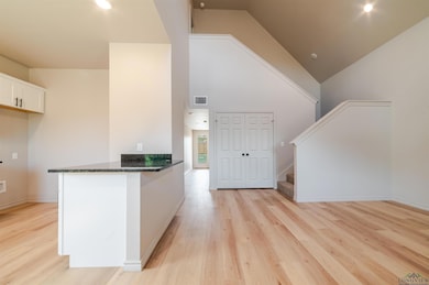 Kitchen featuring light wood-style floors, dark stone countertops, a peninsula, white cabinets, and high vaulted ceiling