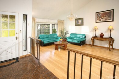 The living room with its soaring ceilings is bathed in natural light from a magnificent bay window and is further accented by a sparkling drop down chandelier and complementary hardwood floors.