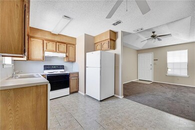 Kitchen with light colored carpet, a textured ceiling, ceiling fan, white appliances, and sink