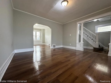 Empty room with dark wood-type flooring, arched walkways, stairway, and crown molding